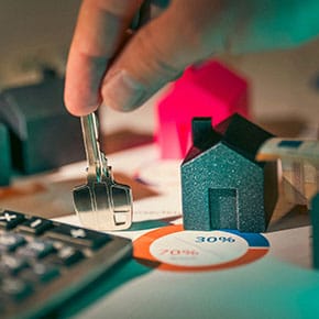 A hand holding a key next to a miniature house